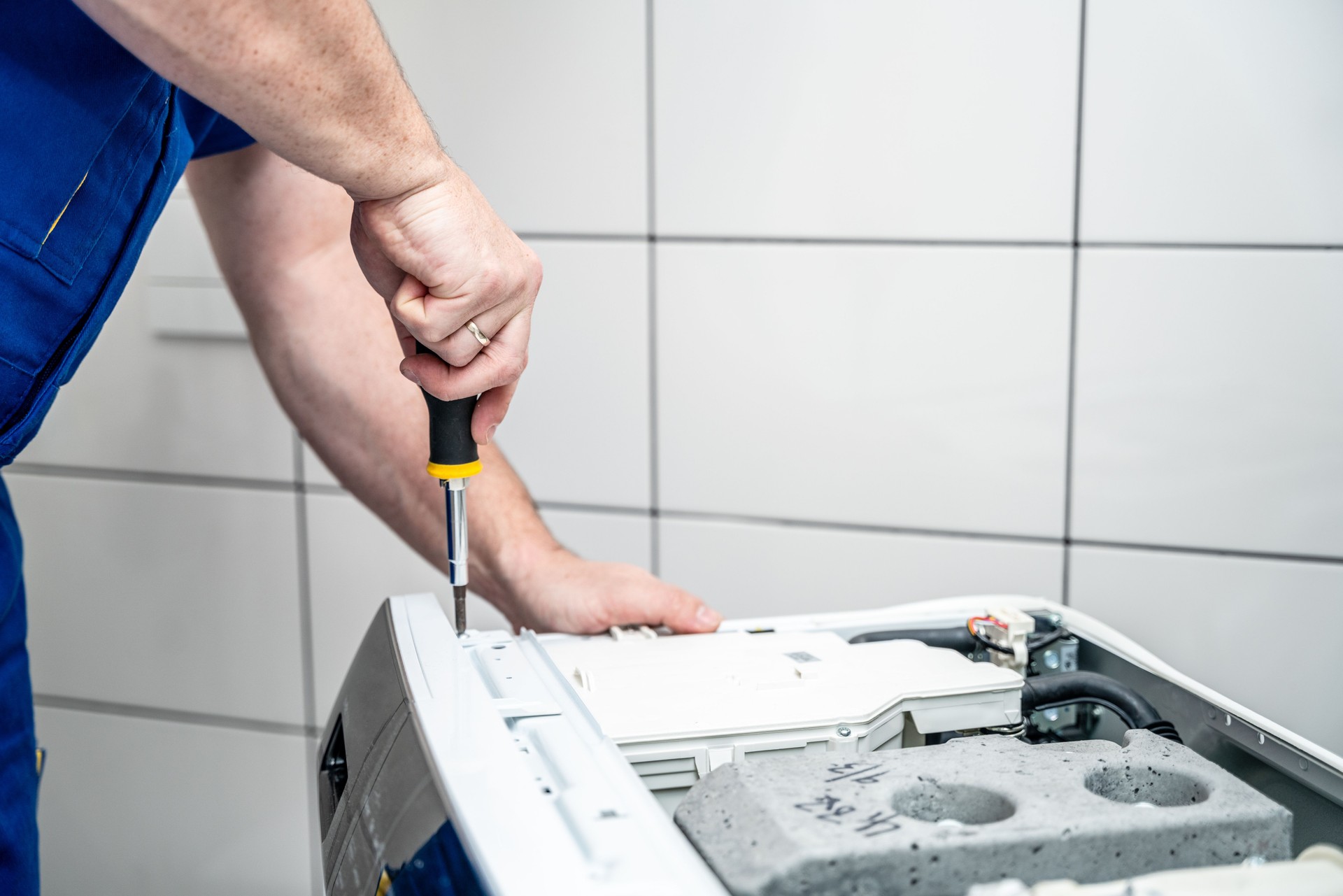 Repairman using a screwdriver disassembles a washing machine for repair